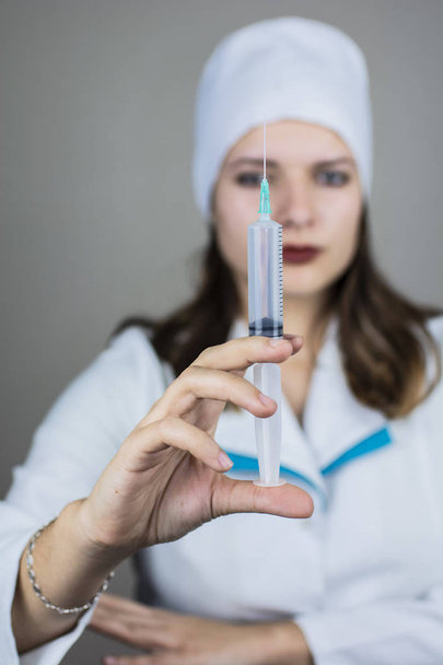 lekarz kobieta w białym fartuchu z ciemnymi włosami w medycznej niebieskiej masce trzyma strzykawkę w dłoniach na jasnym tle - Zdjęcie, obraz