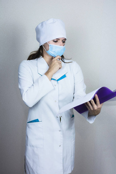 Ärztin in medizinischer Maske sucht Papier auf weißem Hintergrund  - Foto, Bild