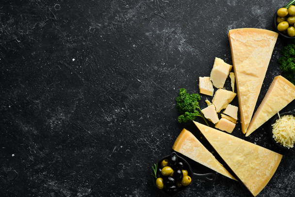 Parmesan. Pieces of Parmesan cheese on black stone background. Top view. Free space for your text. - Foto, afbeelding