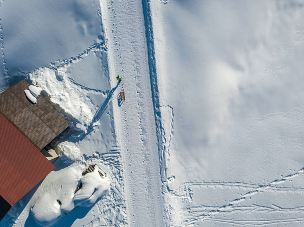 Вид с воздуха на молодую женщину, тащащую сани по снегу
 - Фото, изображение