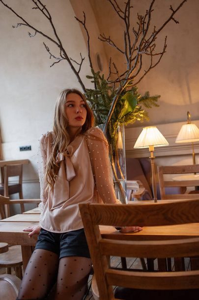 young pretty woman in cafe. grunge. Girl in a cafe in a beige blouse - Фото, зображення