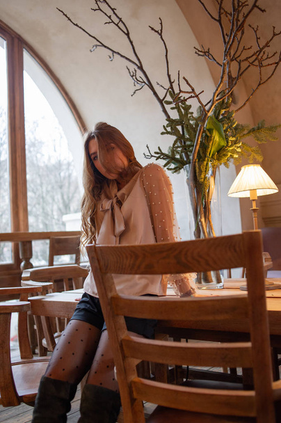 Una joven y bonita mujer en la cafetería. Grunge. Chica en un café en una blusa beige
 - Foto, Imagen