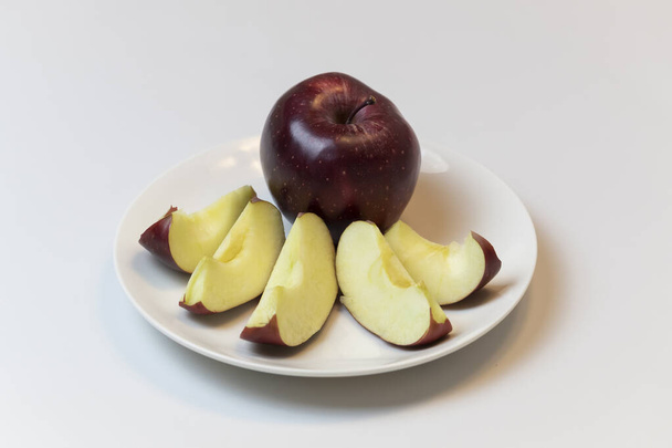 Червоне ціле яблуко і нарізане яблуко на чорнобривцях на білій тарілці зі світлим фоном
. - Фото, зображення