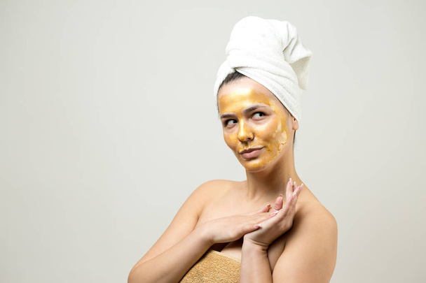 Piękny portret kobiety w białym ręczniku na głowie ze złotą maską odżywczą na twarzy. pielęgnacja skóry oczyszczanie ekologiczne kosmetyki spa relaks koncepcja. - Zdjęcie, obraz