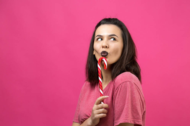 Portrait of lovely sweet beautiful cheerful woman with straight brown hair trying to bite red candy cane christmas. - Photo, Image