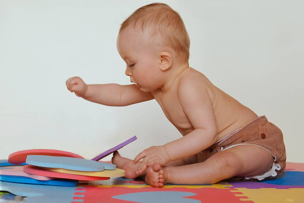 Lindo niño jugando con rompecabezas de espuma y sentado en las esteras de colores
.  - Foto, imagen
