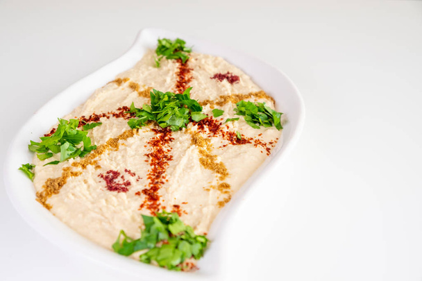 Homemade humus on a white plate with tahini, spicy, olive oil, lemon, parsley and chickpeas. Arabic food, appetizer - Delicious humus. Selective focus. - Foto, afbeelding