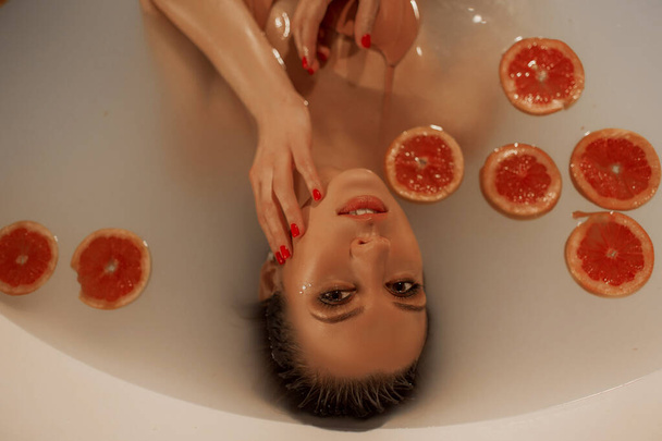 Sexy mladá žena s perfektní pletí ve vaně s mlékem a kruhy grapefruitu - Fotografie, Obrázek