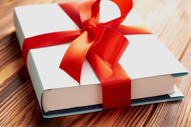 Close-up of a hardback book and blue cover, gift ribbon on a wooden background: concept of a good book - a good gift - Photo, Image