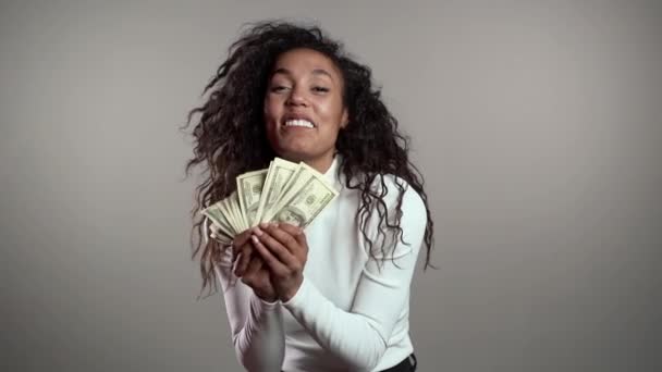 Zadowolona podekscytowana afrykańska kobieta pokazująca pieniądze - banknoty dolarów amerykańskich na szarej ścianie. Symbol sukcesu, zysku, zwycięstwa. Zwolniony ruch - Materiał filmowy, wideo