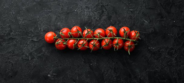 Cherry tomatoes on a twig, on a black stone background. Top view. free space for your text. Rustic style. - Fotó, kép