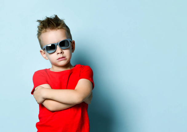 Serious boy in bright stylish casual clothing and sunglasses standing over blue background - Valokuva, kuva