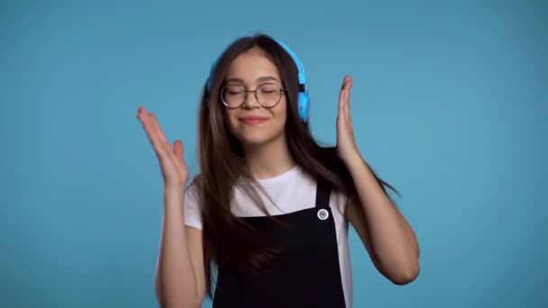 Pretty young asian girl with long hair having fun, smiling, dancing with headphones in studio against blue background. Music, dance, radio concept, slow motion - Imágenes, Vídeo