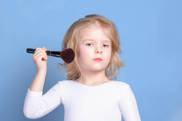 Little girl with blond hair. A beautiful child is powdered with a makeup brush. - Photo, Image