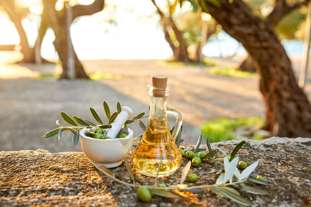 Glasflasche mit Olivenöl und frischen Oliven und Blätter im Freien  - Foto, Bild
