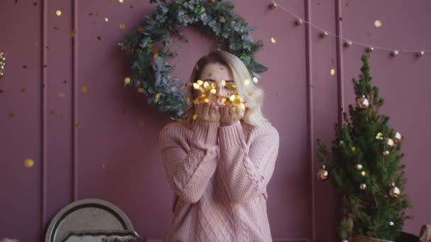 Beautiful woman in sweater blows shiny confetti from her hands to the camera in slow motion, christmas atmosphere, falling golden confetti, new year eve, christmas selebration, Full HD 120fps Prores - Footage, Video