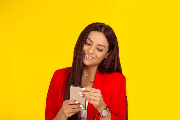 Woman smiling while texting on smartphone, happy news on phone. Mixed race model isolated on yellow background with copy space. Horizontal image. Natural, no makeup. - 写真・画像