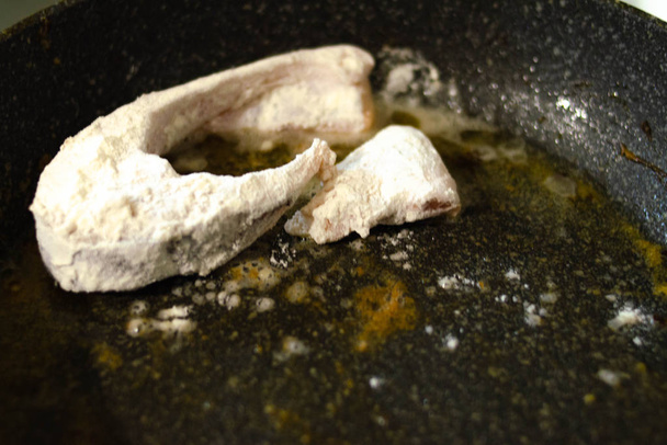 Hal a tésztában. A lisztben lévő haldarabokat vajas serpenyőben sütik. Égés. Veszély Vacsora sült hal. - Fotó, kép