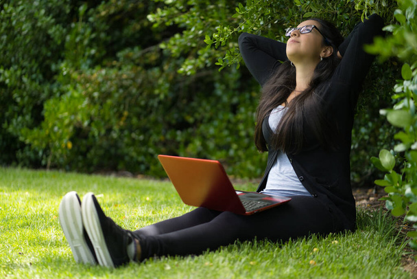 Femme brune s'étirant alors qu'elle est assise sur l'herbe d'un parc. Environnement naturel
 - Photo, image