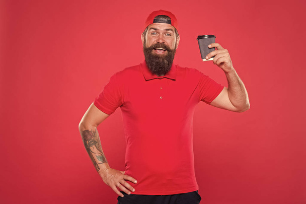 Cheerful barista. Man bearded hipster red cap uniform hold paper coffee cup. Barista recommend caffeine beverage. Barista job position. Coffee shop staff wanted. Barista prepared drink for you - Foto, afbeelding