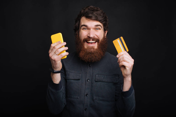 Портрет изумленного молодого человека со смартфоном и кредитной картой
 - Фото, изображение