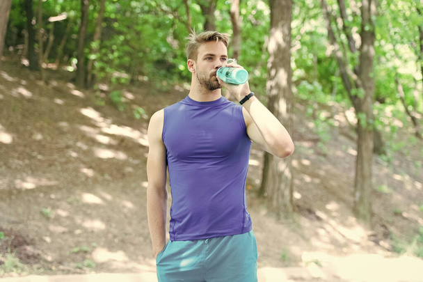 The water has a major role in sports. Thirsty sportsman drinking pure water on hot summer day. Fit athlete having a drink from water bottle during training outdoor. Keeping body water balance - Фото, зображення