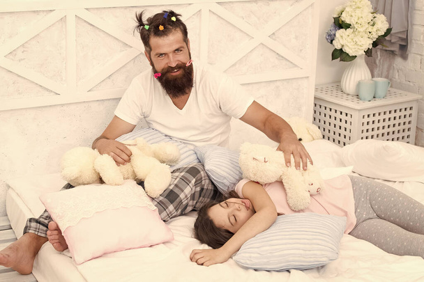 Ending of crazy evening. Having fun pajamas party. Slumber party. Happy fatherhood. Dad and girl relaxing bedroom. Pajamas style. Father bearded man funny hairstyle ponytails and daughter in pajamas - Fotoğraf, Görsel