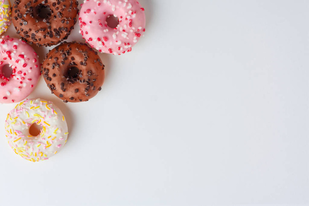 Colorful donuts with different glaze in the corner on white background close with copy space. Junk sweets. - Фото, изображение