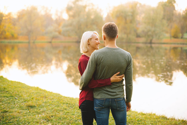 Foto de pareja joven y feliz abrazándose al atardecer cerca del lago durante
 - Foto, imagen