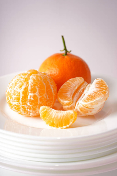 Свежий очищенный и спелый мандарин на белых тарелках на сером фоне. Крупный план
. - Фото, изображение
