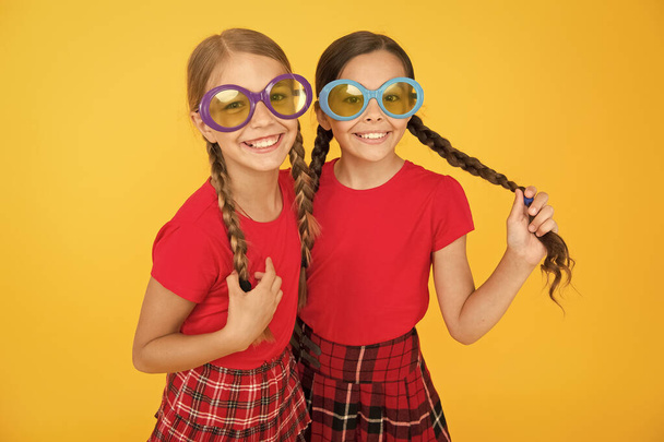 Kids fashionable friends posing in sunglasses on yellow background. Summer fashion trend. Summer fun. Summer accessory. Girls cute sisters similar outfits wear colorful sunglasses for summer season - Foto, imagen