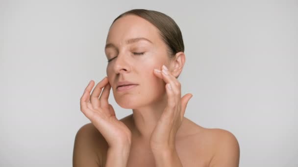 Close-up beauty portrait of young woman with smooth healthy skin, she gently touches her face with her fingers on white background and smiles - Metraje, vídeo
