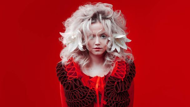 Shades of red. Strange attractive woman in a red outfit, on a red background, with lily flowers in her hair. - Foto, imagen