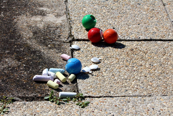 Colorful chalk pastels in various sizes next to plastic balls left on stone tiles at family house backyard - Photo, Image