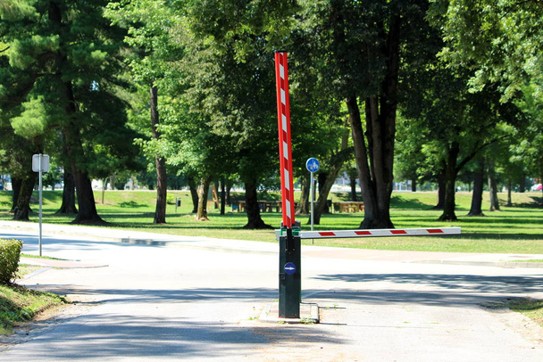 Deux rampes métalliques automatiques à rayures rouges et blanches fermées et ouvertes avec station d'identification et caméras de sécurité à l'entrée du stationnement local pavé entouré d'herbe et d'arbres
 - Photo, image
