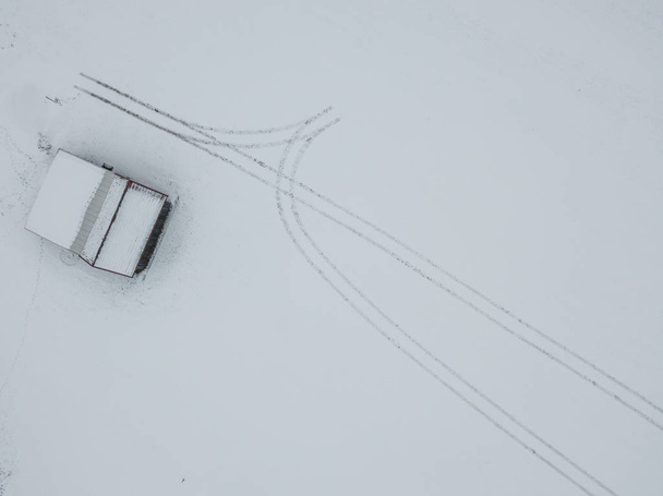 Αεροφωτογραφία ιχνών στο χιόνι που οδηγεί σε ξύλινη καλύβα - Φωτογραφία, εικόνα