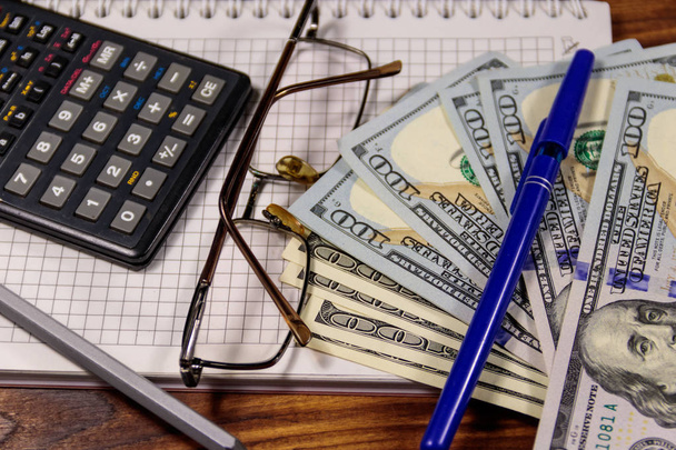 Notebook with dollars, pen, glasses and calculator on wooden desk. Financial concept. Business accounting - Foto, Imagem