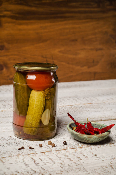 Jar of fermented cucumbers and hot pepper sauce pot close-up. - Фото, изображение