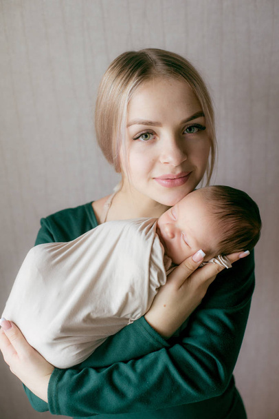 Μια νεαρή, όμορφη ξανθιά, με ένα μωρό στην αγκαλιά της, στο σπίτι. Ευτυχισμένη μητρότητα - Φωτογραφία, εικόνα