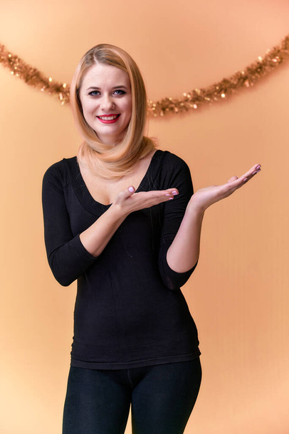 Portrait of a cute girl in a black T-shirt with long beautiful hair and great makeup. Concept of a young blonde woman with New Year's decor. Smiling, showing emotions on a pink background. - Foto, Bild