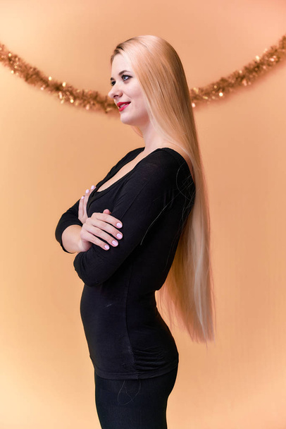 Portrait d'une jolie fille dans un T-shirt noir avec de longs beaux cheveux et un excellent maquillage. Concept d'une jeune femme blonde au décor de Nouvel An. Souriant, montrant des émotions sur un fond rose
. - Photo, image