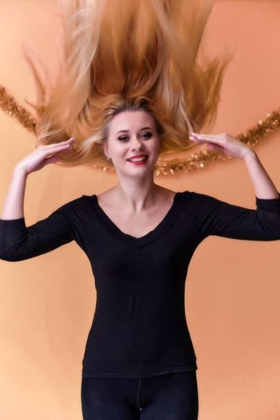 Portrait of a cute girl in a black T-shirt with long beautiful hair and great makeup. Concept of a young blonde woman with New Year's decor. Smiling, showing emotions on a pink background. - Foto, Imagem