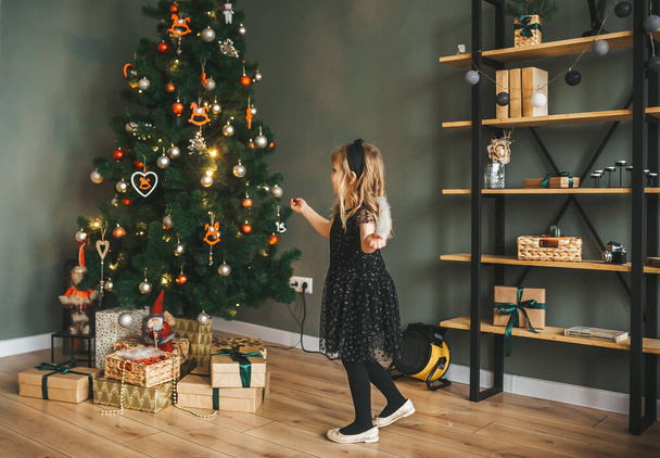 ein kleines Mädchen hat Spaß im festlichen Wohnzimmer in der Nähe des Weihnachtsbaums - Foto, Bild
