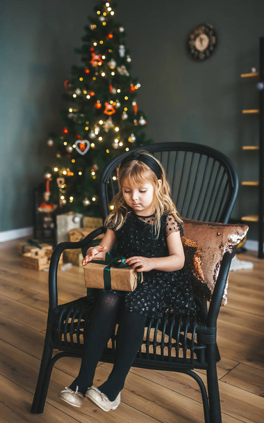 Mooi meisje met de doos van de gift in handen zitten in de stoel kerst interieur - Foto, afbeelding