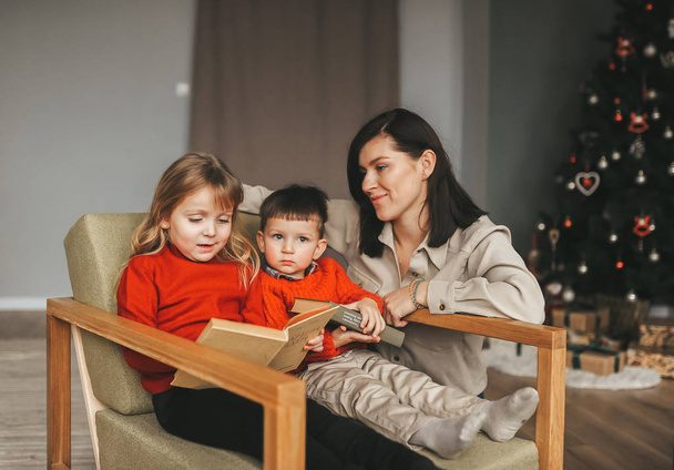 Moeder met kinderen in nieuwjaar interieur lezen boek. - Foto, afbeelding