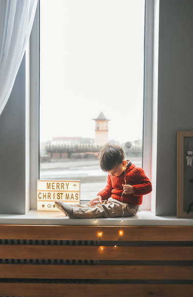 Παιδί κάθεται στο περβάζι του παραθύρου και κοντά Διοικητικό Συμβούλιο με την επιγραφή Καλά Χριστούγεννα - Φωτογραφία, εικόνα