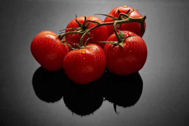 Зображення пучка свіжих помідорів на чорному тлі з відображенням і краплями води
 - Фото, зображення