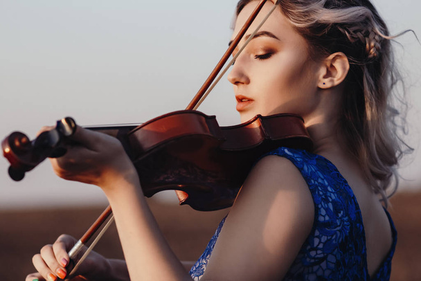 face of a beautiful girl with a violin under her chin outdoors, young woman playing a musical instrument on nature in solitude, concept music and feelings - Foto, Imagem