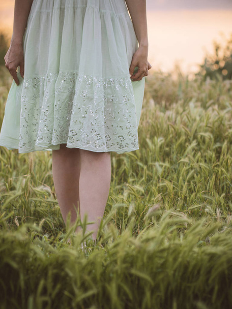 young girl walks alone in a field in summer, the legs of a young girl in a modest dress walk in the grass, a romantic melancholy mood - Photo, image