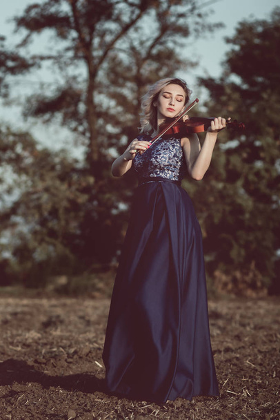 face of a beautiful girl with a violin under her chin outdoors, young woman playing a musical instrument on nature in solitude, concept music and feelings - 写真・画像